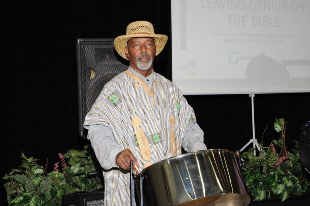 Man in traditional attire playing a steel drum outdoors at night.