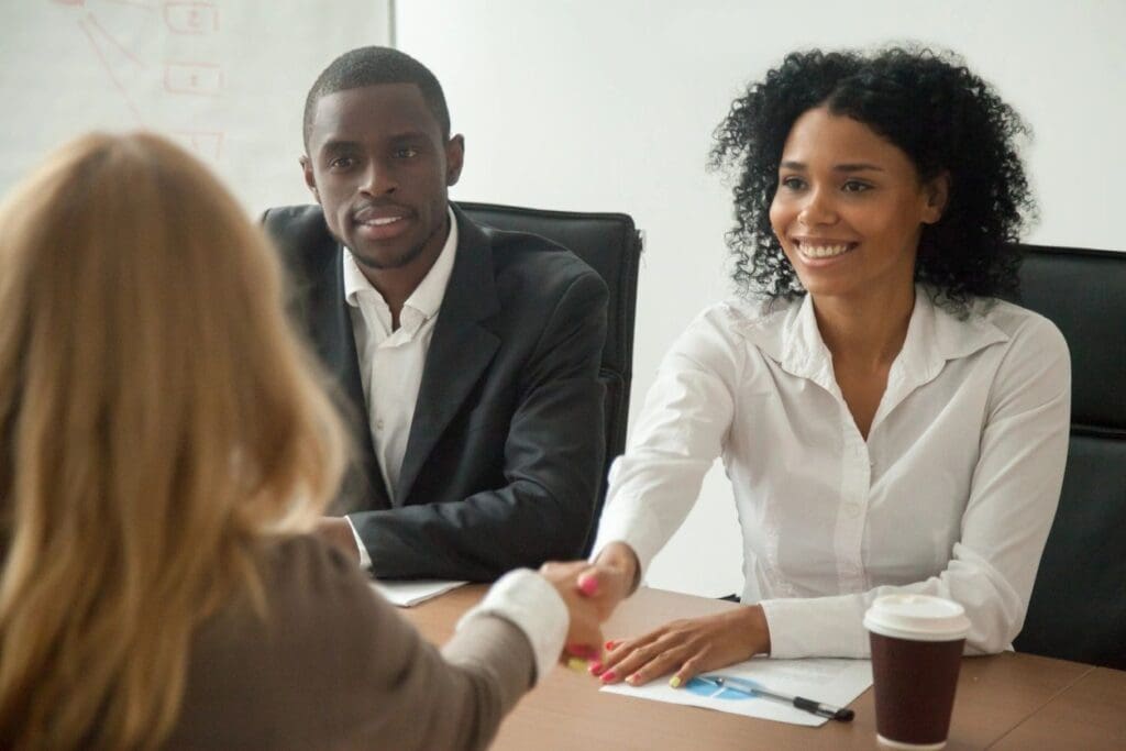 Two professionals shaking hands during a meeting with a colleague.