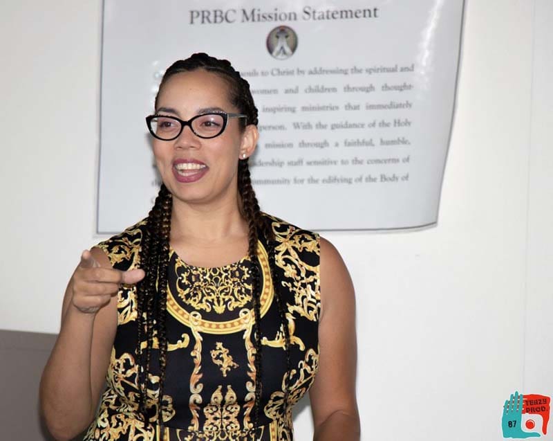A woman wearing glasses and a patterned dress speaking or presenting.