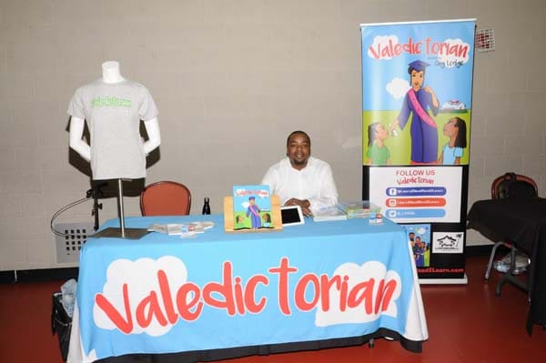 A man sitting behind a valedictorian display table at an event.