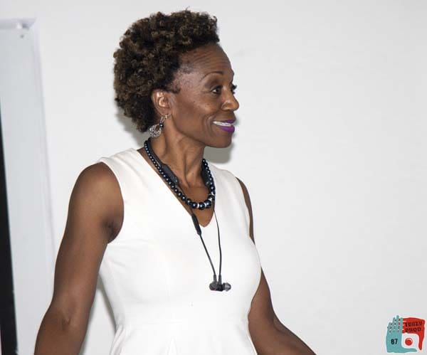 Woman in a white sleeveless top smiling and looking sideways.