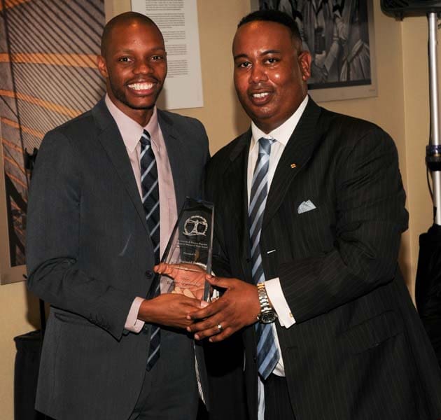 Two men in suits exchanging an award at an event.