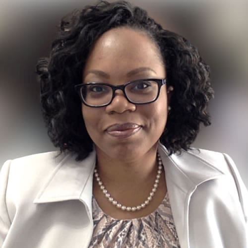 Professional woman wearing glasses and a white blazer, smiling.