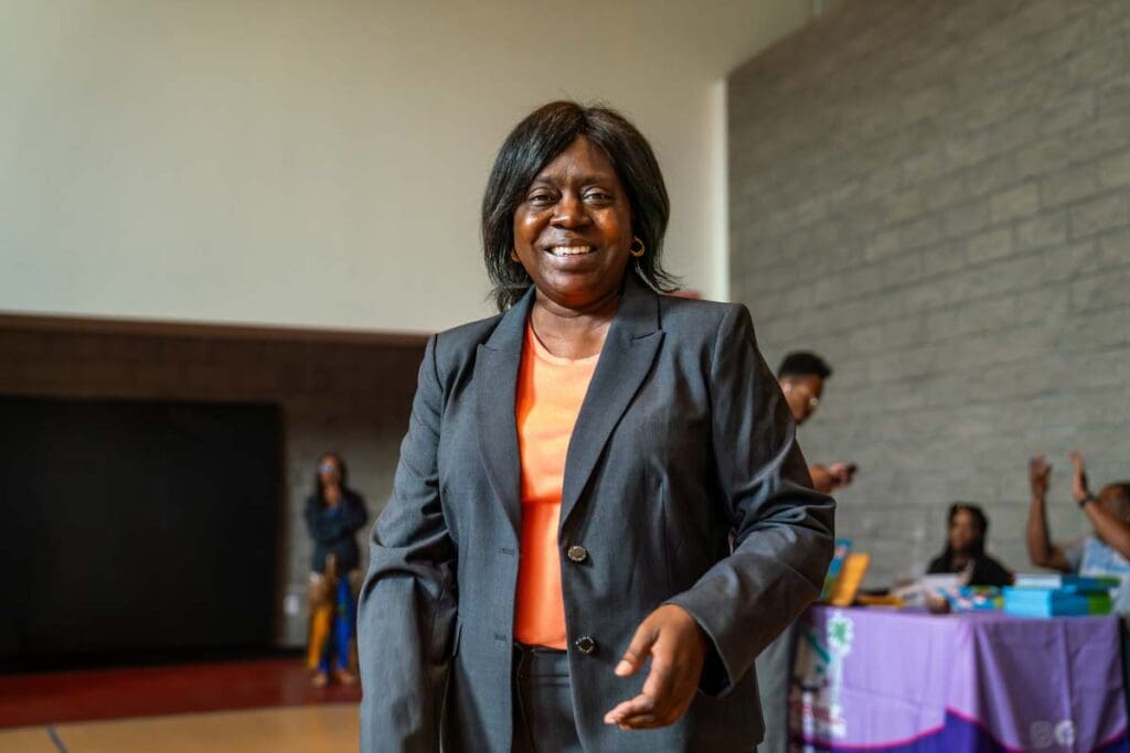 A smiling woman in a black blazer and orange top indoors.