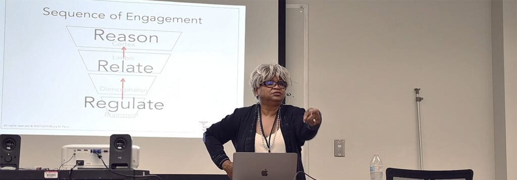 A woman with gray hair presenting in front of a projection screen.