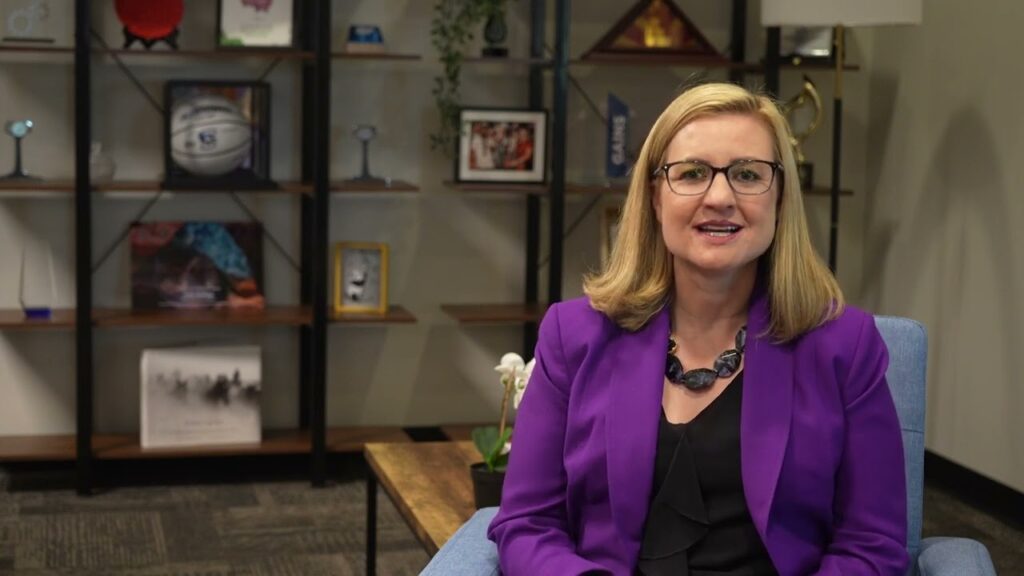 Woman in purple blazer sitting indoors.