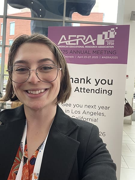 Person smiling in front of conference sign.