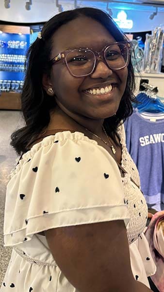 Smiling woman wearing glasses and heart-patterned dress.