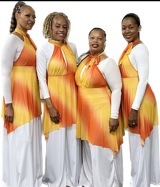 Four women in coordinated orange and white dresses pose together.