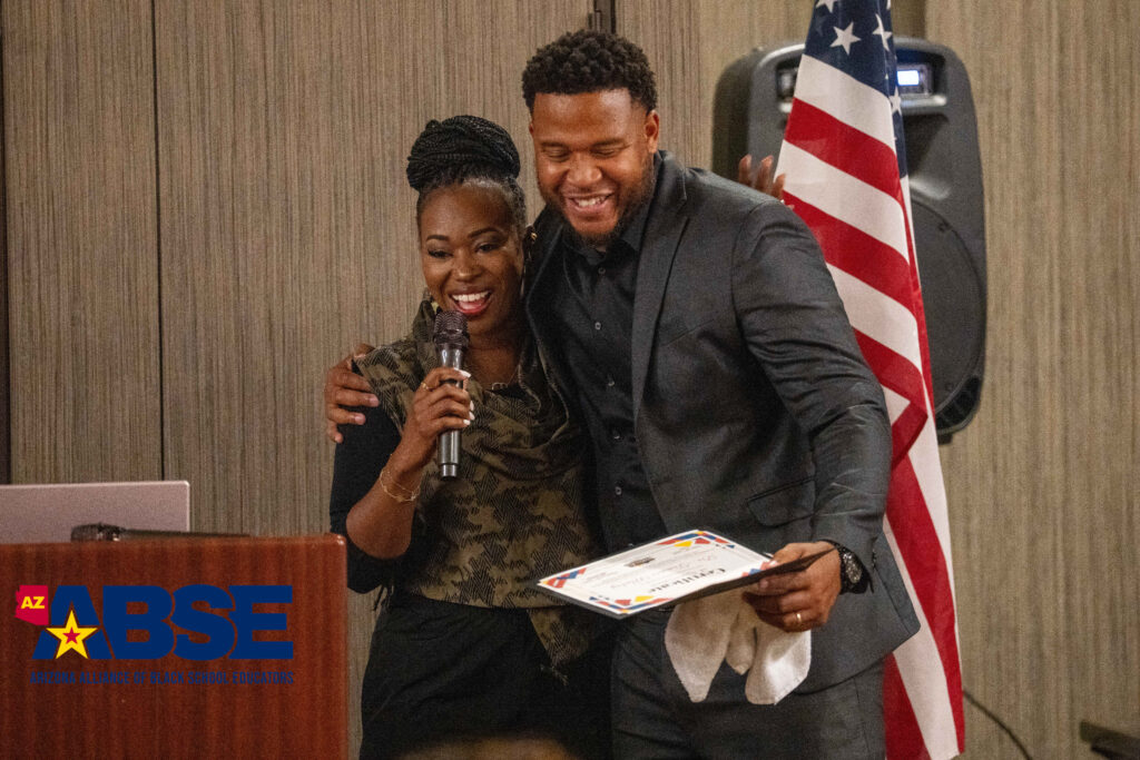 Two people smiling and holding a certificate with an American flag in the background.