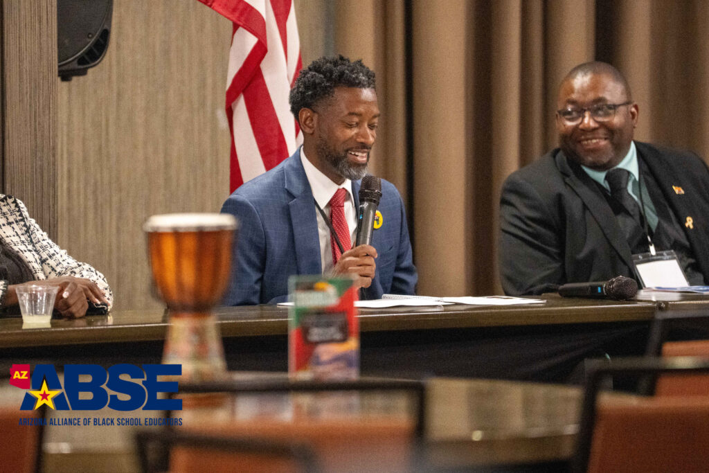Two men in suits at a formal meeting with an American flag in the background.