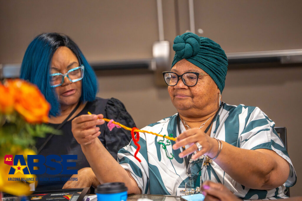 Two women engage in a creative hands-on activity involving string and sticks.